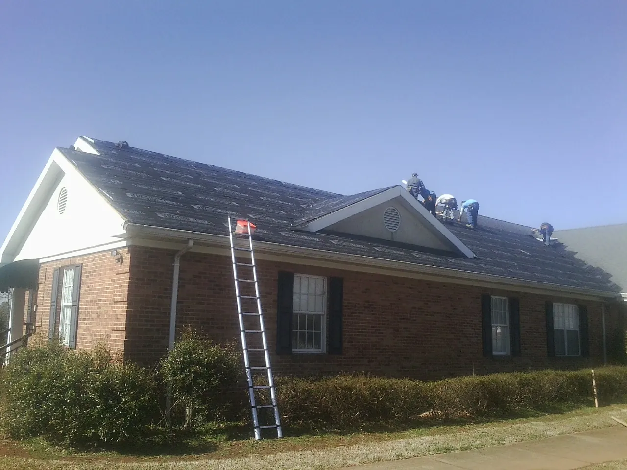 Crew tearing shingles off a brick ranch roof with a ladder set — Emergency Roof Repair work by our crew in Duncan