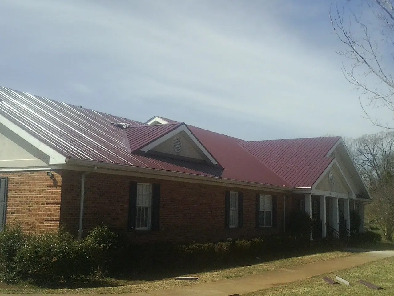 Red metal roof with gabled entries on a long brick building, from a Hail Damage Roof Repair job in Duncan