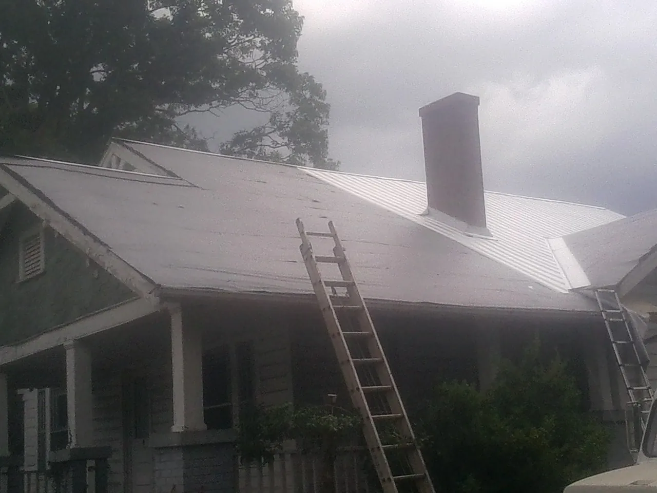 Ladders against a metal roof on an older home with a brick chimney in Duncan