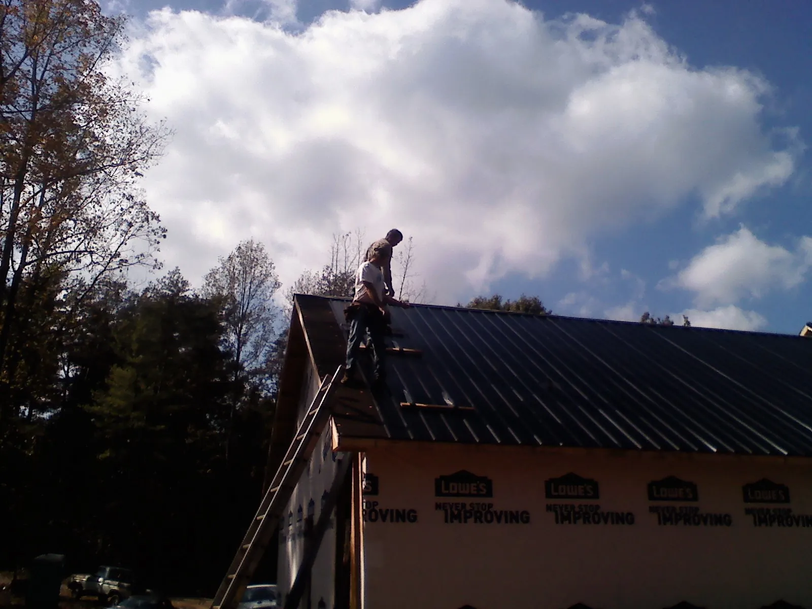 Roofer fastening dark metal panels high against a cloudy sky, from a Roof Inspection job in Duncan