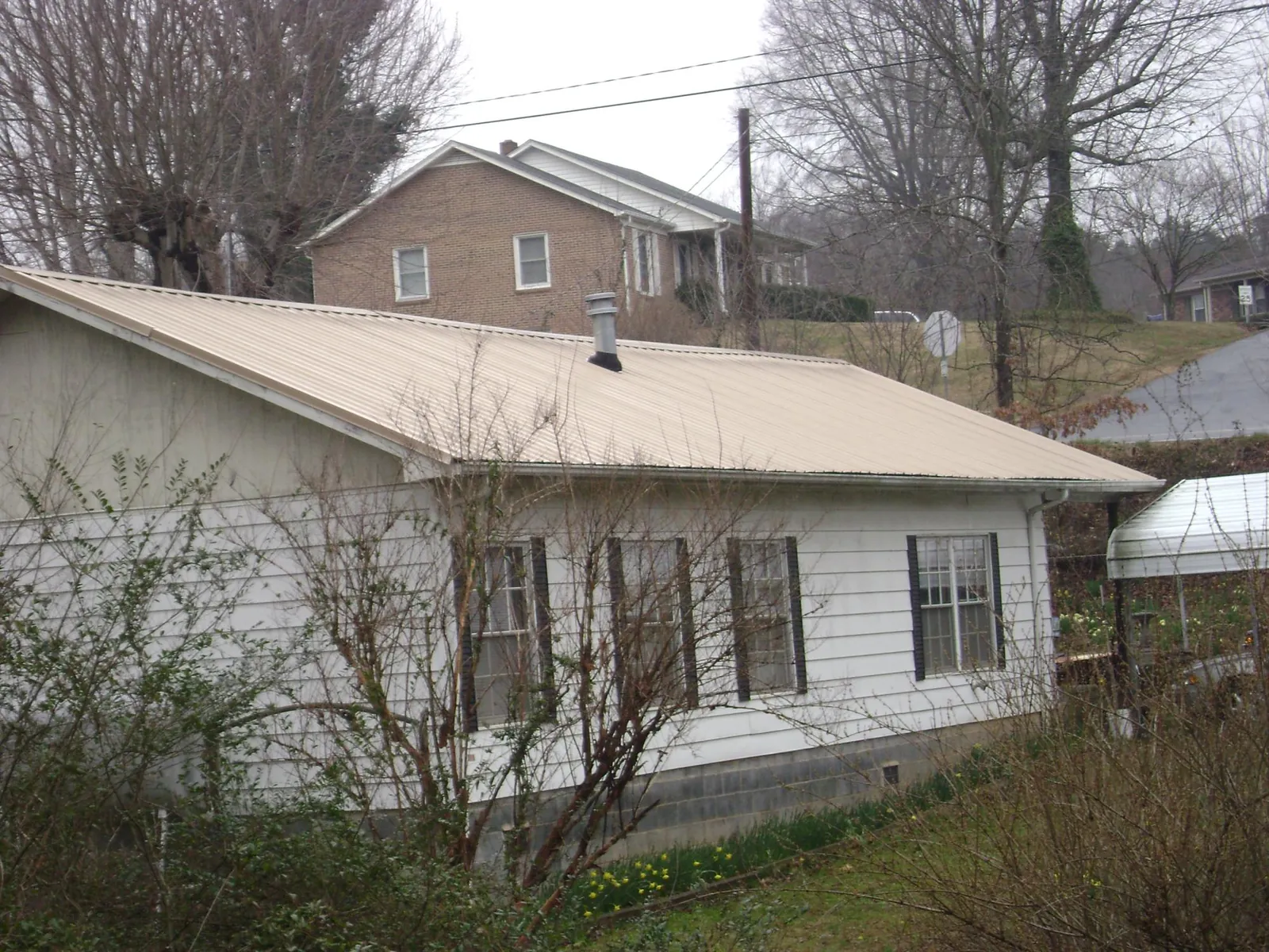 Tan metal roof on a white sided house set into a hillside — Commercial Roofing by Roofing Brothers in Duncan
